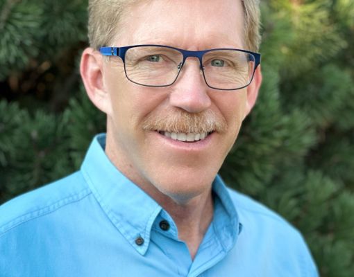 Smiling individual in a blue shirt against a green background
