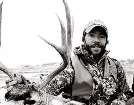 Hunter posing with a mule deer in a natural setting.