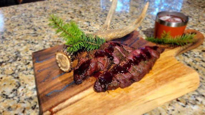 Plate of venison with antler decoration on wooden cutting board.