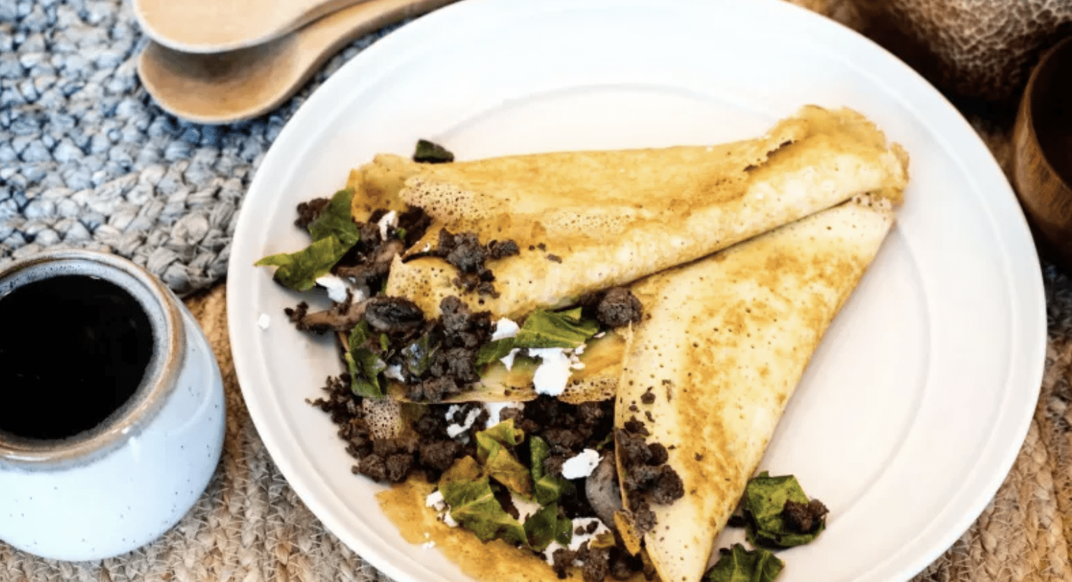 Savory crepe filled with meat and greens on a plate.