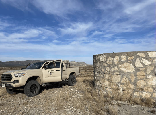 Pick-up truck near water storage in open desert landscape.