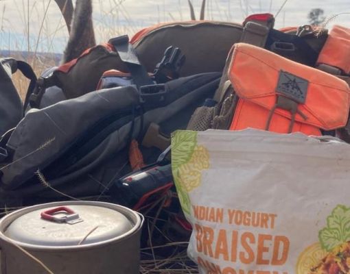Hunting gear and cookware in a field with a mule deer antler.