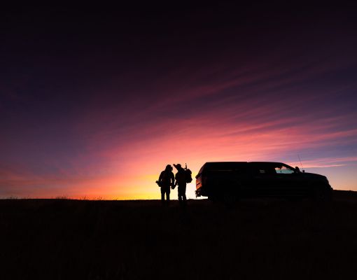 Silhouettes of a hunting party at sunset with a vehicle