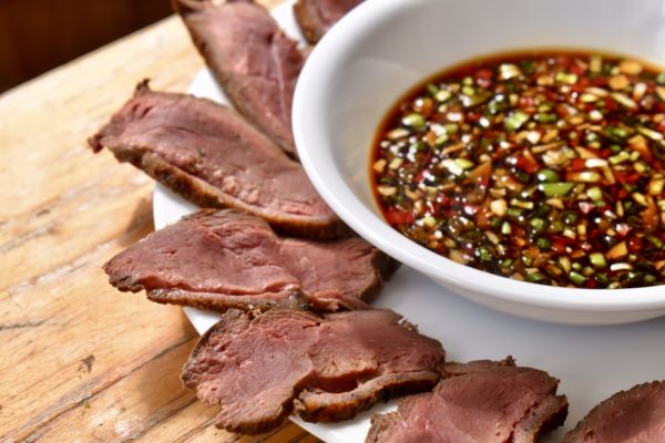 Slices of venison served with a flavorful dipping sauce on a wooden table.