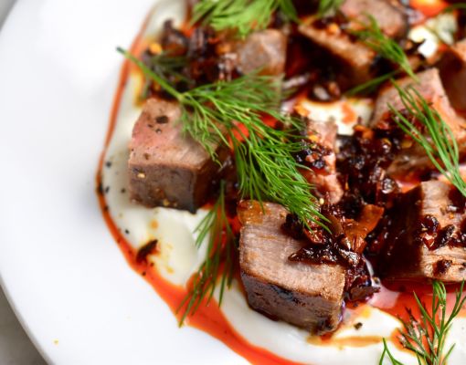 Plated venison dish garnished with herbs and sauce.