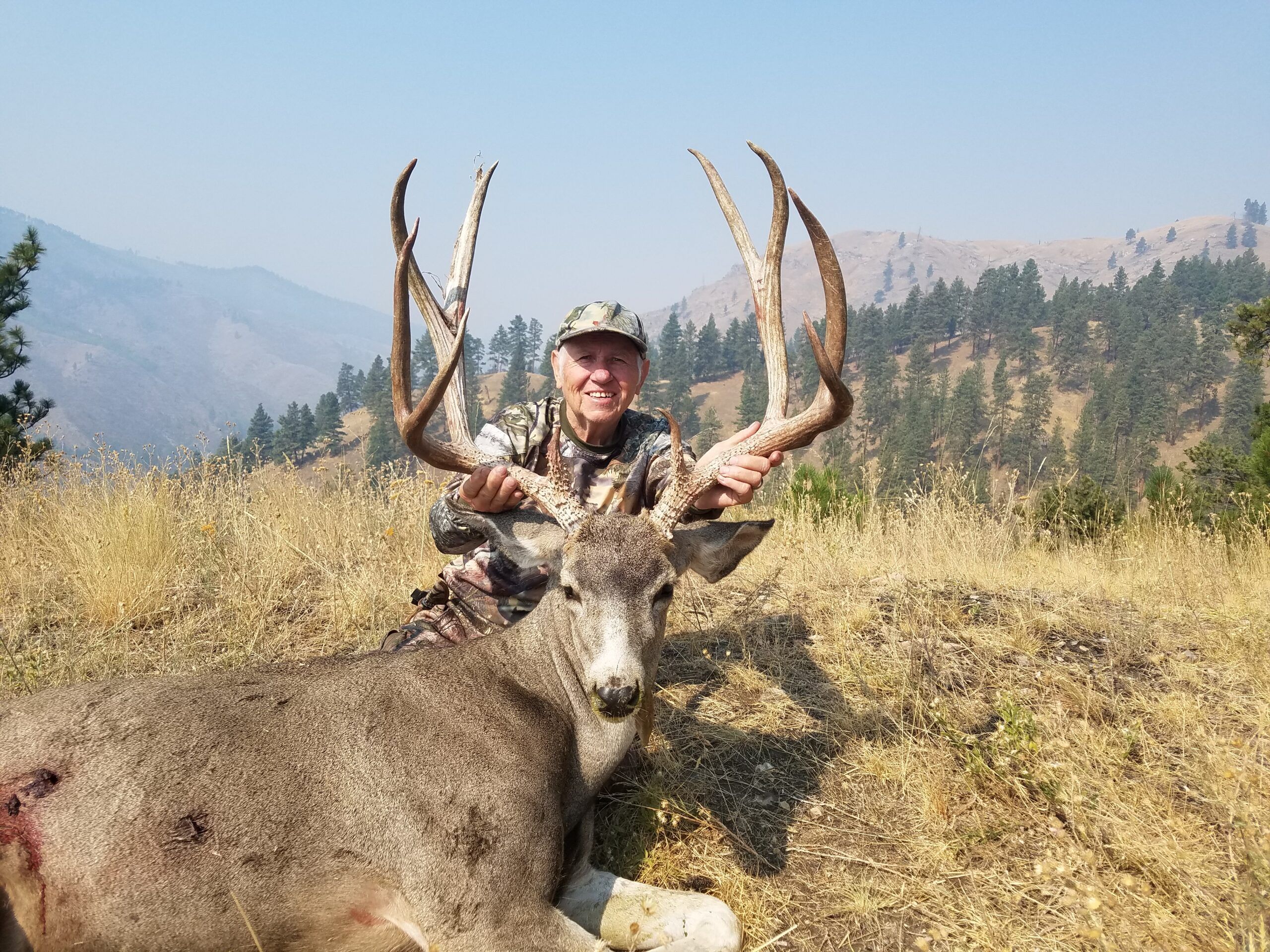Hunter with a mule deer buck in a mountain setting.