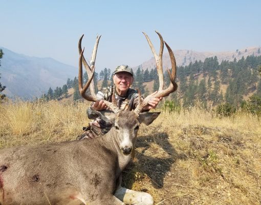 Hunter with a mule deer buck in a mountain setting.