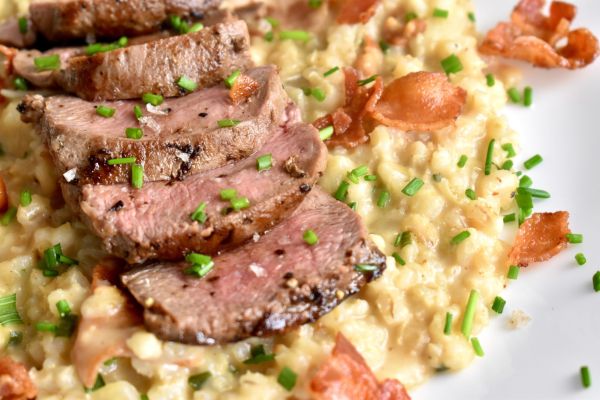 Sliced mule deer steak served with rice and garnished with chives.
