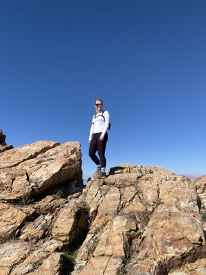 Hiker standing on rocky terrain under clear blue sky.