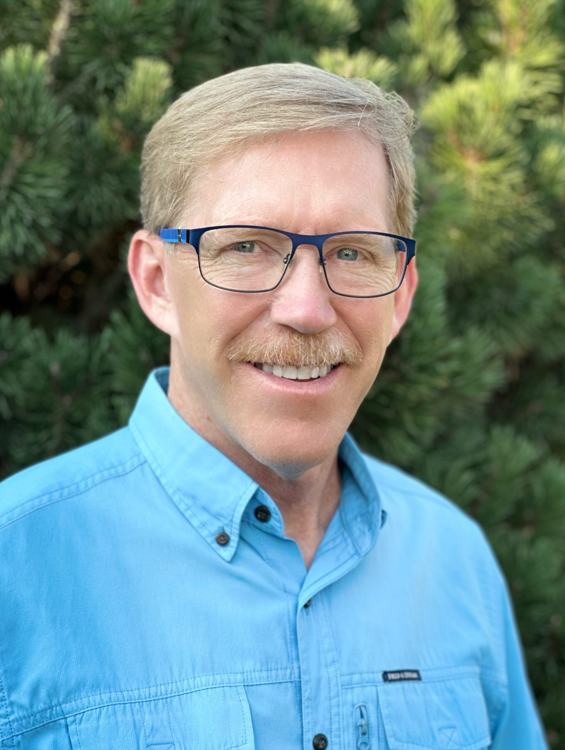 Smiling individual in a blue shirt against a green background