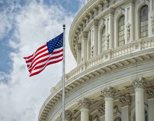 U.S. Capitol building with flag against a blue sky.