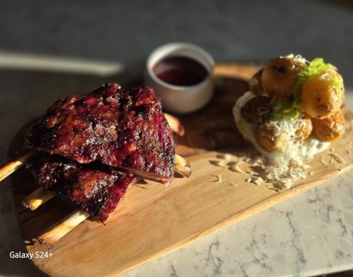 Grilled ribs served with a side dish and sauce on a wooden platter.