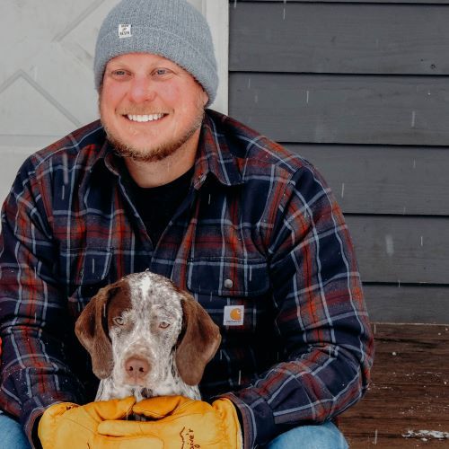 Man with brown and white hunting dog in snowy weather.