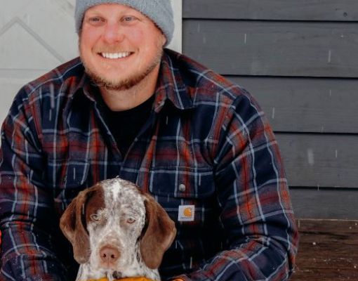 Man with brown and white hunting dog in snowy weather.