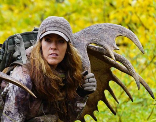 Woman hunter carrying moose antlers in vibrant autumn landscape.