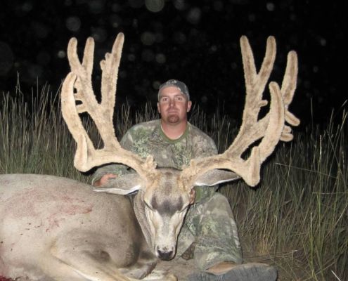 Hunter with large mule deer buck at night.