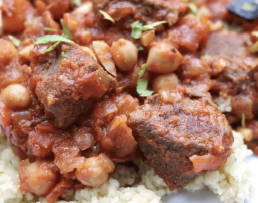 Venison stew served over grain, garnished with herbs.