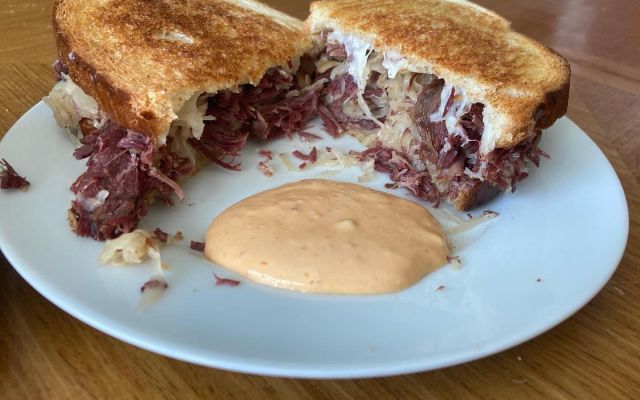 Corned beef sandwich with sauerkraut and dipping sauce on a white plate.