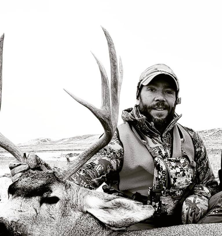 Hunter posing with a mule deer in a natural setting.