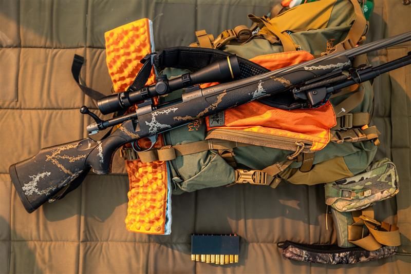 Hunting gear including a rifle, backpack, and ammunition on a padded surface.
