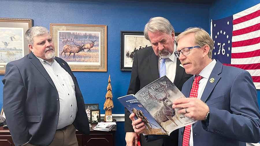 Three men discussing a publication about the Mule Deer Foundation.