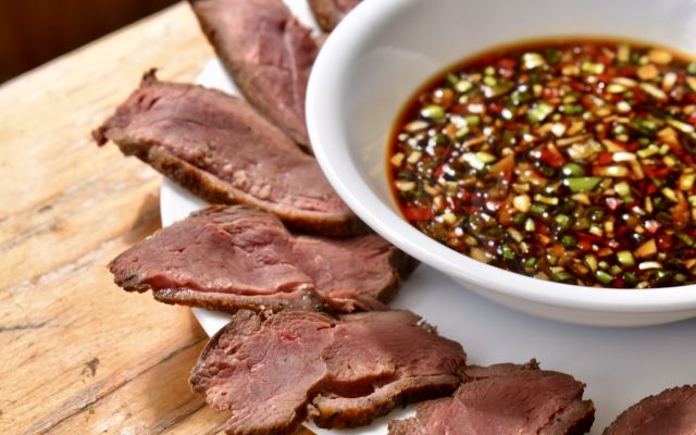 Slices of venison served with a flavorful dipping sauce on a wooden table.