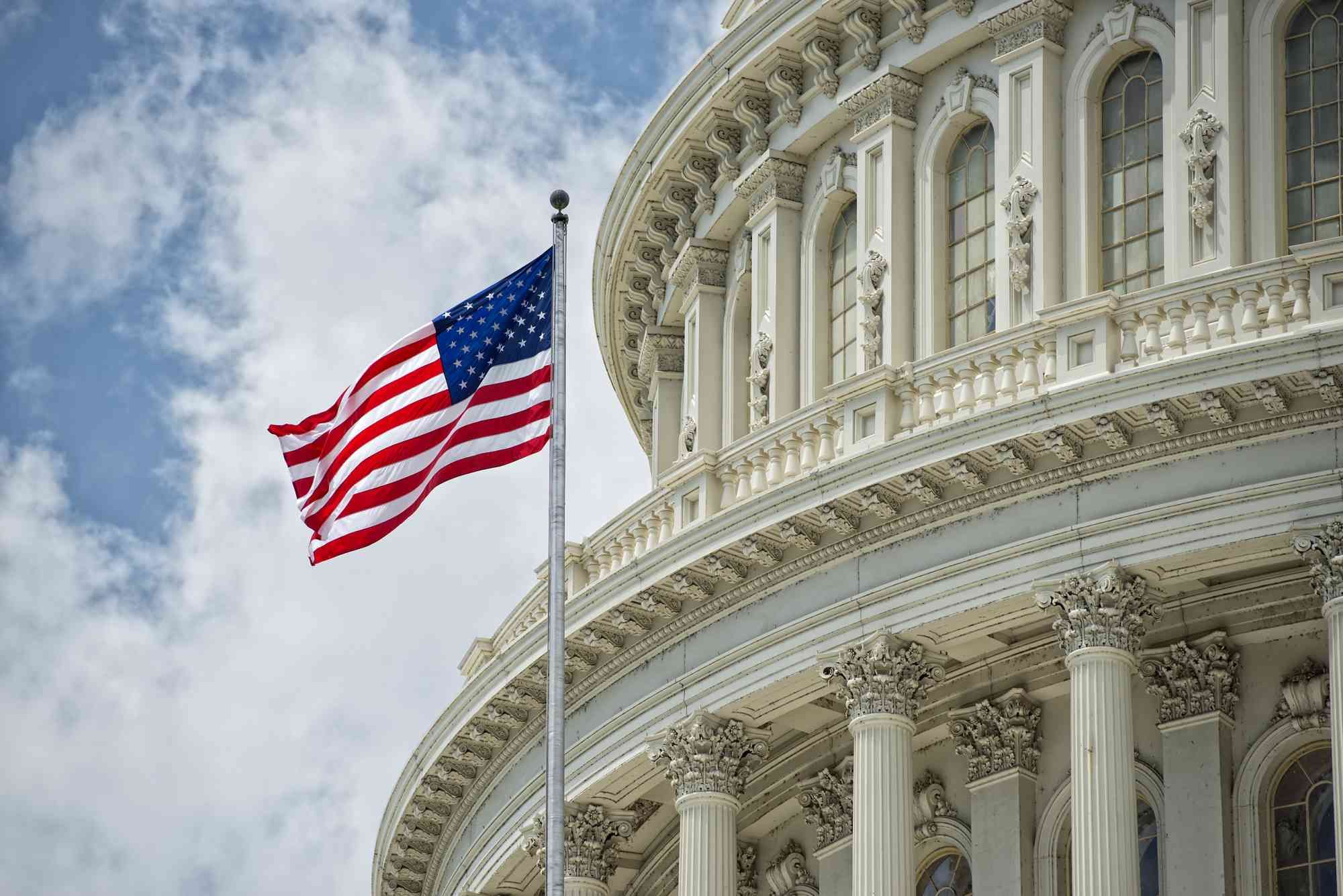 U.S. Capitol Building with American flag against cloudy sky.