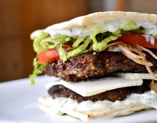 Gourmet burger featuring layers of vegetables and sauce.