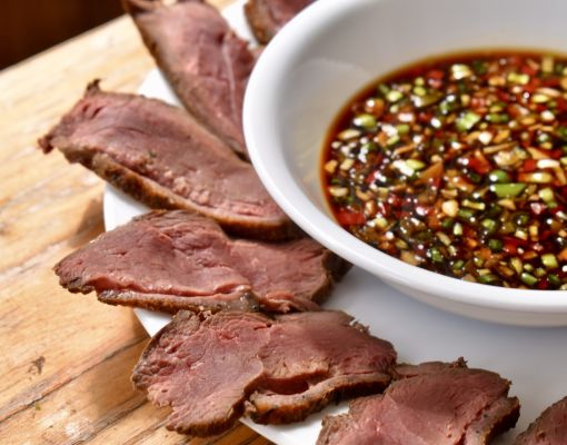 Slices of venison served with a flavorful dipping sauce on a wooden table.