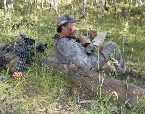 Hunter in camouflage resting and writing notes in a forest setting