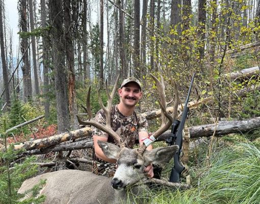 Hunter with mule deer in a forest setting.