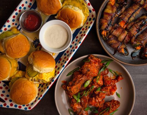 Delicious food platter featuring sliders, hot wings, and bacon-wrapped peppers.