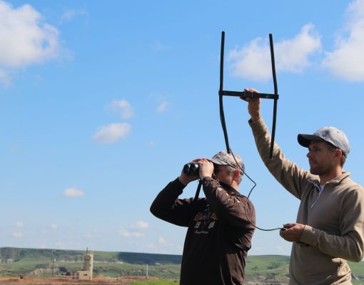 Researchers conducting wildlife telemetry in open field with blue skies.