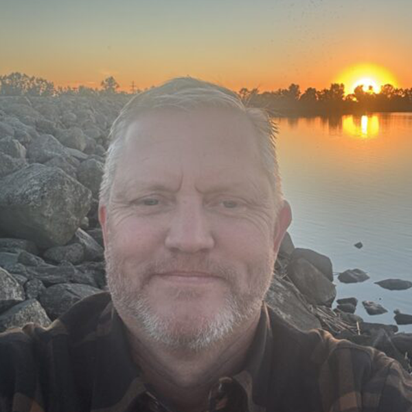 Man posing for a selfie by a lake during sunset.