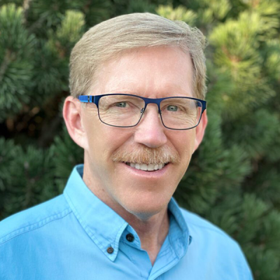 Outdoor portrait of a smiling individual wearing glasses.