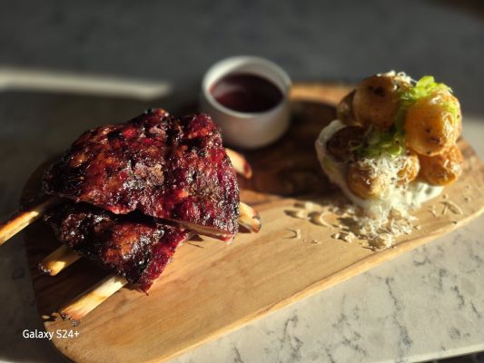Grilled ribs served with a side dish and sauce on a wooden platter.