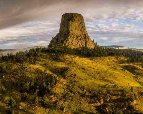 Devils Tower National Monument surrounded by forest and grasslands.