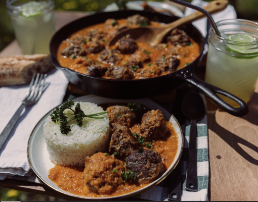 A plate of beef meatballs in tomato sauce with rice on a wooden table.