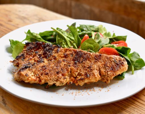 Grilled fish filet served on a plate with fresh spinach and tomato salad.