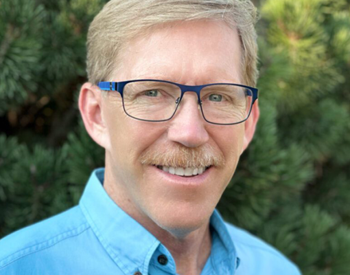 Outdoor portrait of a smiling individual wearing glasses.