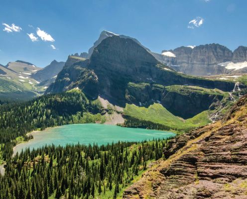 A scenic view of a mountain lake surrounded by tall pine trees and rocky peaks.