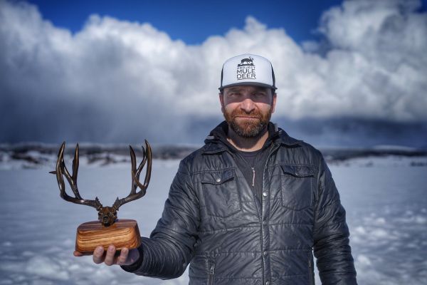 Man holding mule deer antlers trophy in snowy setting