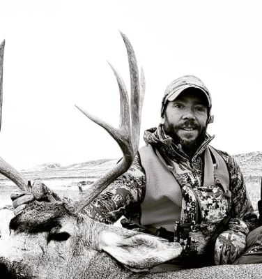 Hunter posing with a mule deer in a natural setting.