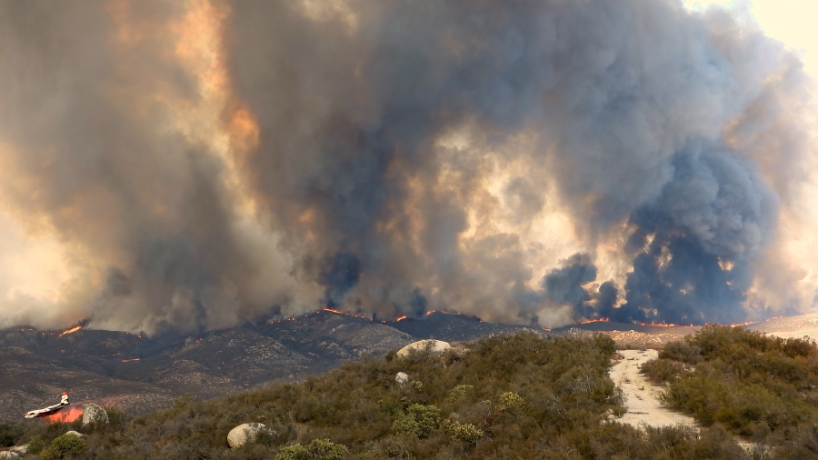 Wildfire in mountain region with smoke and flames.