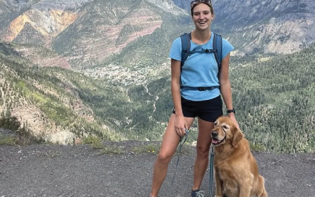 Hiker with a golden retriever enjoying a mountain view.